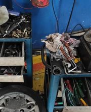 Caixa de ferramentas bagunçada com chaves, peças automotivas, e uma roda de carro no chão.