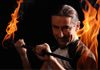 Mann mit Feuerstab, der Flammen in beide Hände hält, in einer dynamischen Pose vor dunklem Hintergrund.