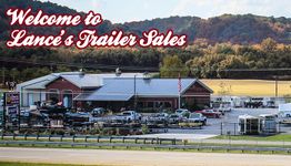 Trailer sales lot with building, inventory, and welcome sign in front of scenic hills.