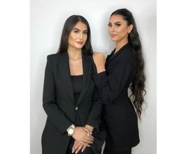 Zwei Frauen in schwarzen Blazern vor weißem Hintergrund, eine blickt zur Seite, eine nach vorne.