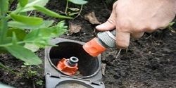 Hand connecting a garden hose to an underground sprinkler system in a garden.