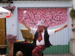 Clown mit Hut und Zauberstab führt vor Kindern auf, bunte Kulisse im Hintergrund.