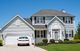 Two-story white house with a garage and a car parked in the driveway under a clear blue sky.