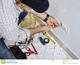 Man installing an electrical outlet on a wall, surrounded by tools and diagrams.