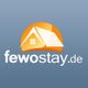 Logo von fewostay.de mit einem Haus und einer Sonne auf blauem Hintergrund.