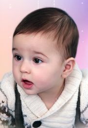 Ein Baby in einem weißen Strickpullover blickt neugierig nach vorne vor einem bunten Hintergrund.
