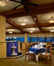 Restaurante elegante con mesas vestidas de azul y blanco, techo con vigas y ventiladores.