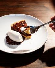 Pessoa cortando torta de chocolate com garfo e sorvete em prato branco sobre mesa de madeira.