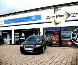 Schwarzes Auto vor einer Autowerkstatt mit der Aufschrift "Auto Point Zeven" auf der Fassade.