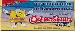 Placa da Distribuidora Cremosinho de Garanhuns com mascote sorridente e telefones para contato.