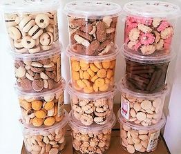 Potes plásticos empilhados com biscoitos variados, incluindo rosquinhas, biscoitos amarelos e rosas.