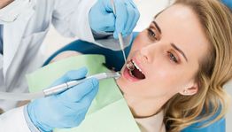 Dentist in blue gloves examines a patient with dental tools.