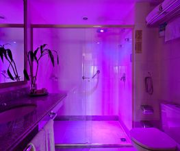 Banheiro com iluminação roxa, espelho amplo, vaso sanitário e chuveiro com box de vidro.
