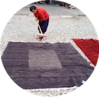 Eine Person kehrt im Freien einen Teppich auf einem Kiesboden.