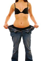 Frau in schwarzem BH trägt zu große Jeans und zeigt Gewichtsabnahme.