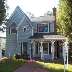 Blue two-story house with neon open signs and white porch surrounded by greenery.
