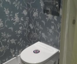 Baño con inodoro blanco y papel tapiz floral azul.