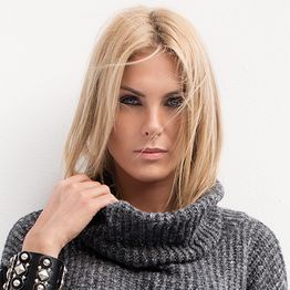 Mulher loira com suéter cinza e pulseira preta, olhando diretamente para a câmera.