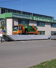 Orange Müllwagen auf Rampe vor dem Entsorgungsfachbetrieb Schmutzler Gebäude, blauer Himmel.