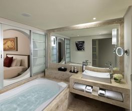 Baño moderno con bañera, lavabo, espejos grandes y puertas correderas hacia el dormitorio.