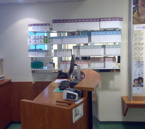 Opticien interieur met balie, computer, brillen bij display, en dozen met lenzen op planken.
