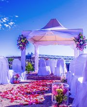 Boda al aire libre con sillas blancas y decoración floral bajo un cielo azul.