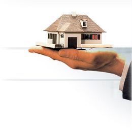 Eine Hand hält ein kleines Modellhaus vor weißem Hintergrund.