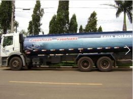 Caminhão-tanque azul de água potável estacionado em rua, com árvores ao fundo.