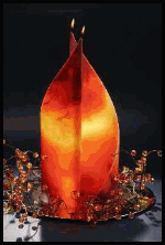 Orange Kerze in Blätterform, brennend, umgeben von kleinen Dekorationsperlen vor dunklem Hintergrund.