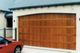 Red car parked in front of a closed wooden garage door attached to a beige building.