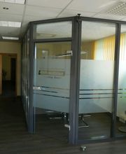Büro mit Glaswänden, dunklem Fußboden und hellem Licht durch Fenster mit gelben Vorhängen.
