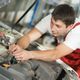 Mechanic in red overalls working on a car engine in a garage.