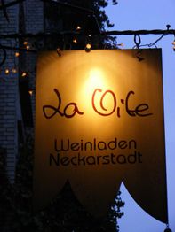 Schild mit Aufschrift "La Vite Weinladen Neckarstadt" beleuchtet im Dunkeln, umgeben von Lichtern.