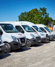 Mehrere weiße Lieferwagen parken auf einem Kiesplatz unter blauem Himmel.