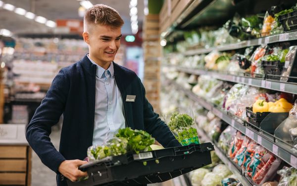 Mann befüllt Supermarktregal mit Salat 