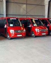 Cinco minibuses rojos estacionados en fila dentro de un garaje.