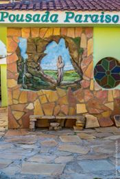 Fachada da Pousada Paraíso com pintura de paisagem e figura religiosa na parede.