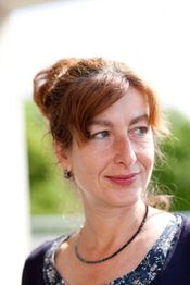 Eine Frau mit roten Haaren schaut lächelnd zur Seite, draußen im Sonnenlicht.