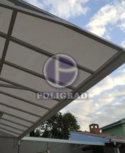 Toldo de metal e vidro com céu azul ao fundo e algumas nuvens claras.