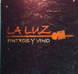 Schild mit der Aufschrift "LA LUZ PINTXOS Y VINO" auf schwarzem Hintergrund.