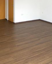 Leerer Raum mit braunem Holzboden und zwei Holztüren an der linken Wand.