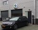 Zwarte auto geparkeerd voor een bedrijfsgebouw met een bord dat "DHZ" aangeeft.