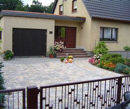 Einfamilienhaus mit Garage, gepflegtem Garten und Pflastersteinen im Hof, geschlossene Tor.