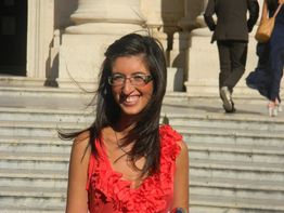 Una donna sorridente in un abito rosso su una scalinata.