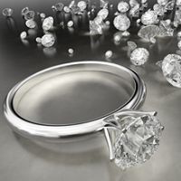 A diamond ring lies on a shiny surface with scattered loose diamonds in the background.