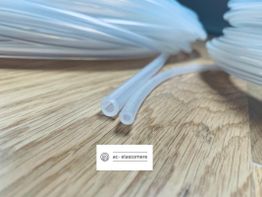 Transparente Schläuche aus Kunststoff auf Holzuntergrund, mittig Logo von ac-elastomere.