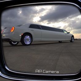 Limousine reflection in side mirror under cloudy sky.