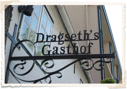 Schild mit dekorativem Schriftzug "Dragseth's Gasthof" an einer Gebäudewand.