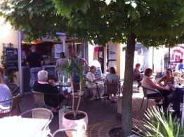 Personen sitzen in einem Café im Freien unter einem Baum. Gemütliche Atmosphäre bei Sonnenschein.