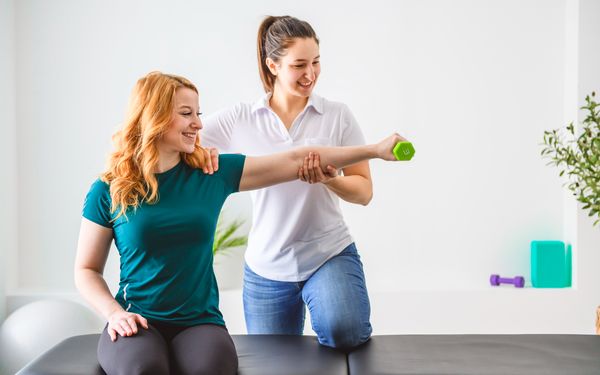 Physiotherapeutin hilft Patientin den Arm zu heben und diesen durch Gewichte zu trainieren.